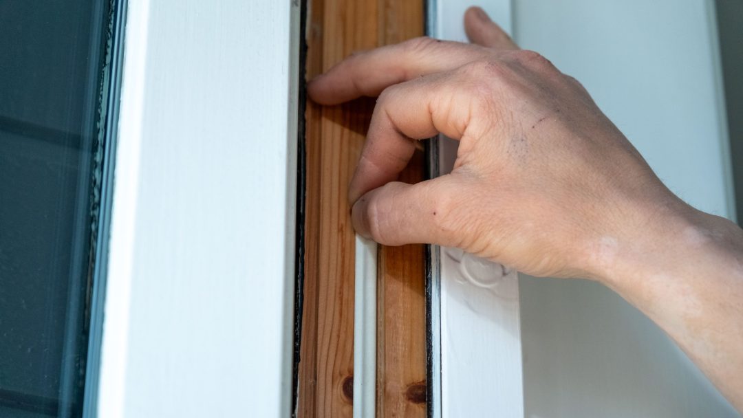 En hånd justerer forsiktig en vindusramme av tre, montere tetningslister dyktig for å sikre en lufttett forsegling.