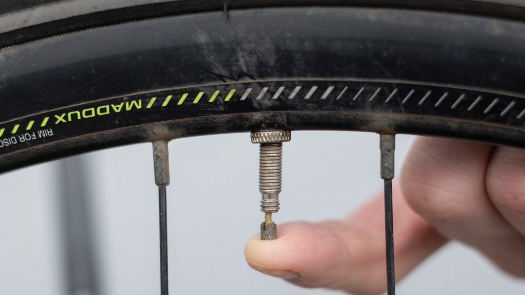 En sykkeldekkventil med en finger som forsiktig trykker på den, omgitt av metalleiker og en del av et oppblåst gummidekk, venter på sitt øyeblikk for å skifte dekk, og sørger for jevne turer fremover.