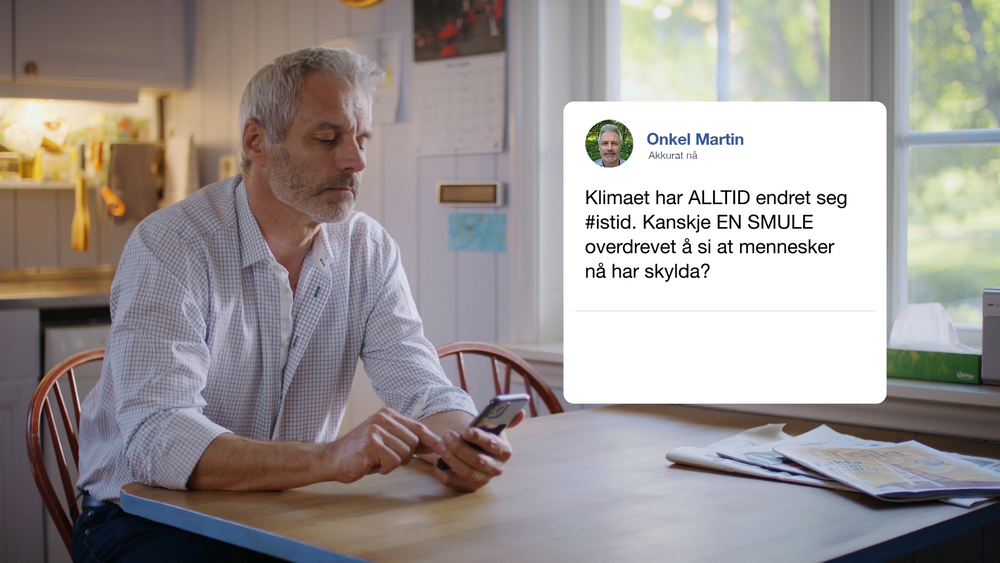 En mann sitter ved et kjøkkenbord og stirrer skeptisk på smarttelefonen sin. Et innlegg i sosiale medier om klimaendringer fanger hans oppmerksomhet, vekker nysgjerrighet og dypere refleksjon.