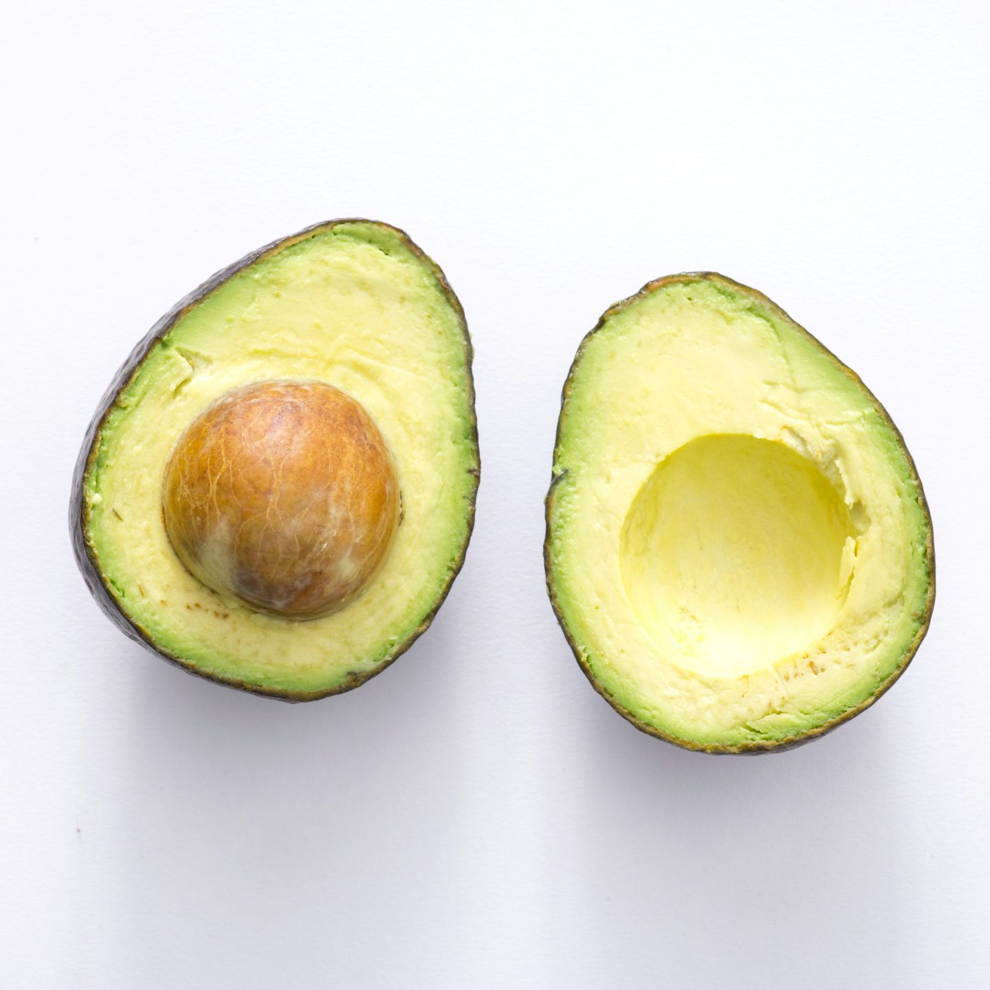 To avokadohalvdeler hviler på en hvit bakgrunn, og viser frem enkelheten til kortreist matte. Den ene halvdelen vugger gropen sin, mens den andre har en glatt overflate der gropen er fjernet.