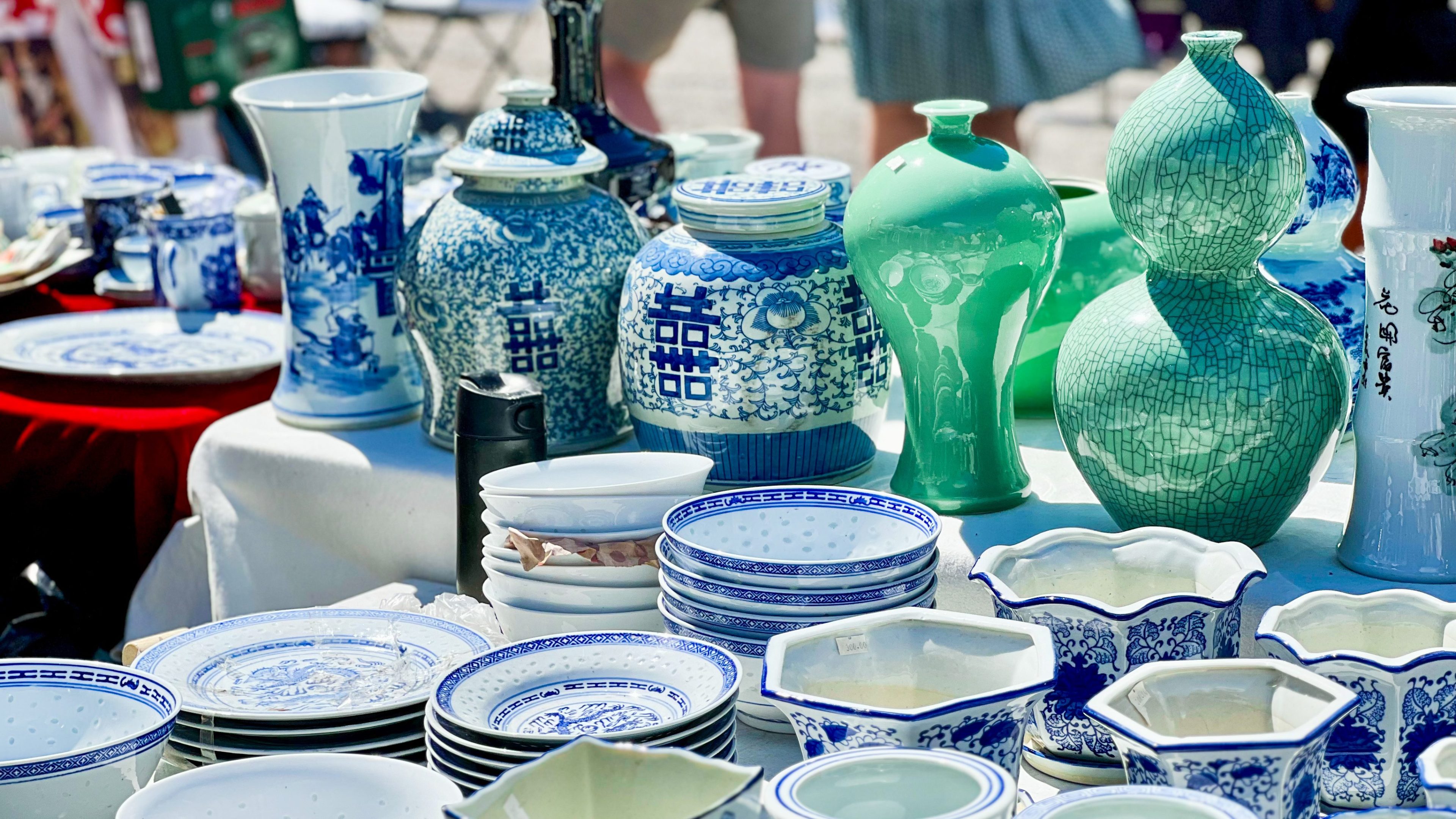 En skattejakt på et utendørsmarked avslører et herlig utvalg av blå og grønne keramiske vaser og fat, vakkert arrangert på et bord.