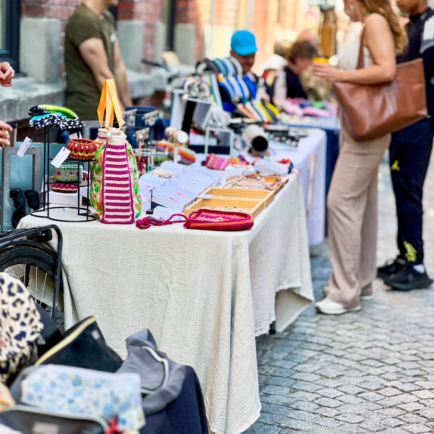 I en livlig utendørs markedsscene er bordene fulle av håndlaget håndverk og unikt tilbehør som lokker globetrottende shoppere. Mot et bakteppe av murvegger og brosteinsbelagte fortau ser folk ivrig gjennom de verdslige skattene som er utstilt.