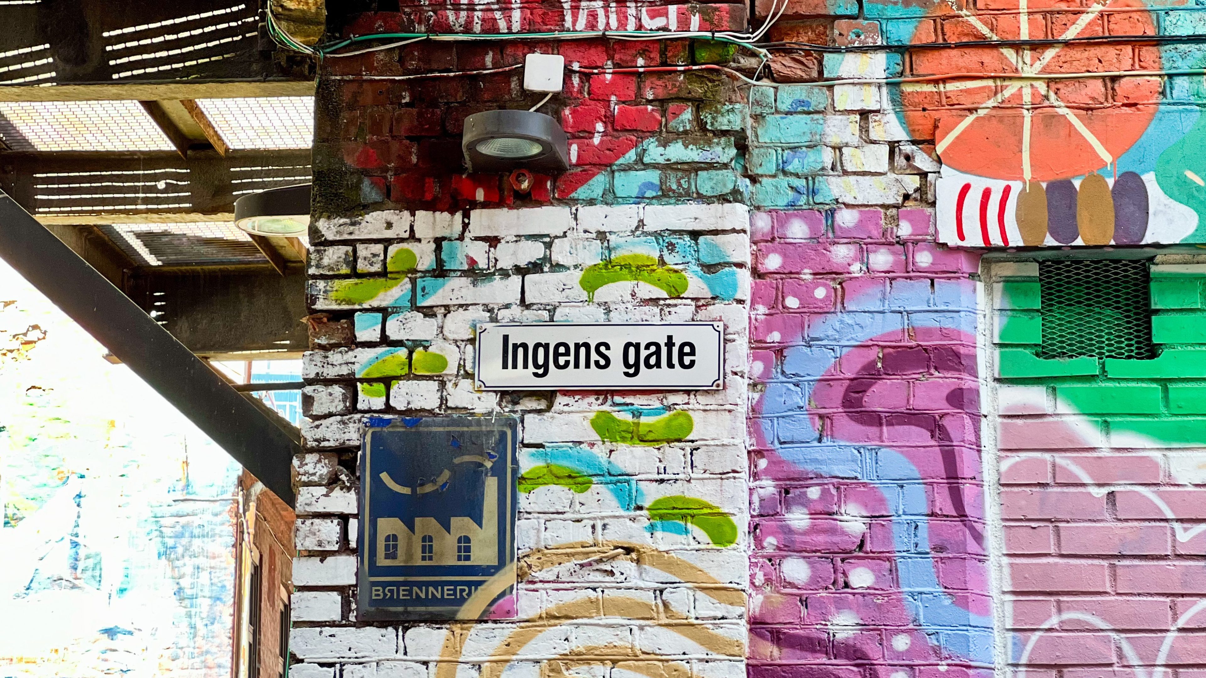 Murvegg med fargerik graffiti, med et gateskilt merket «Ingens gate». En liten plakat under viser en bygning og ordet BIENNER, som antyder en skjult skattejakt.