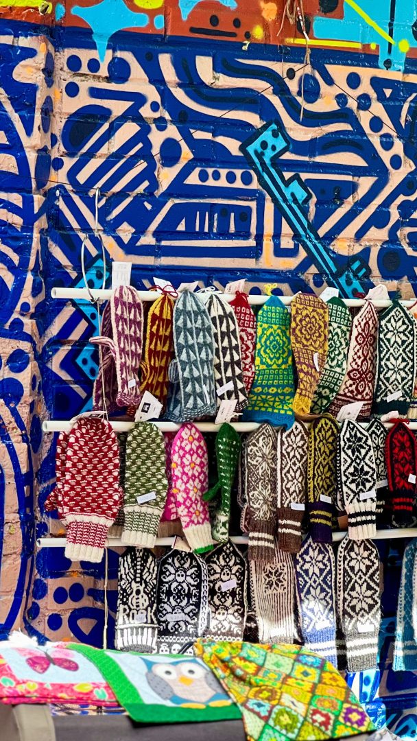 Fargerike strikkede votter vist på et stativ foran en levende, geometrisk graffitivegg gir en uventet vri på denne urbane skattejakten.