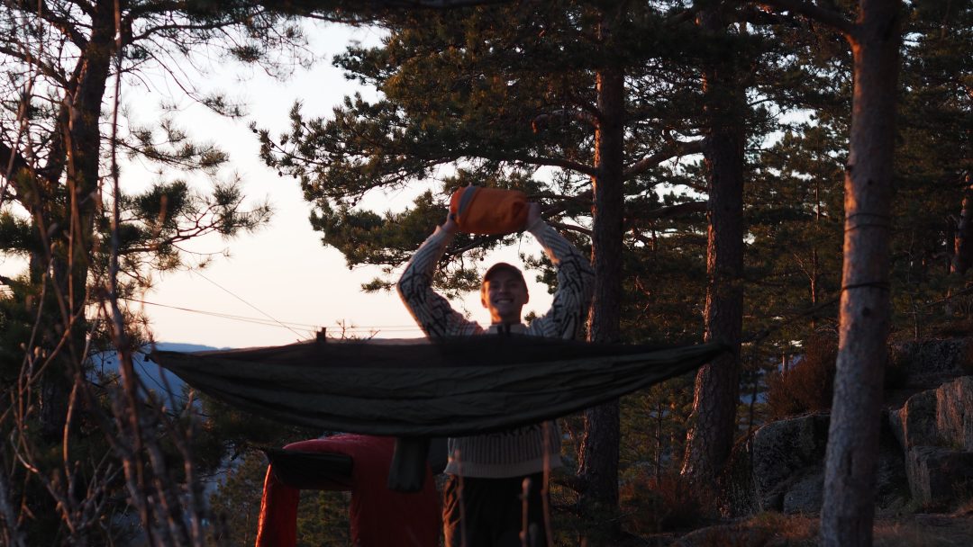 Ved solnedgang blir en person telt opp i den rolige skogen, metodisk setter han opp en hengekøye blant trærne.