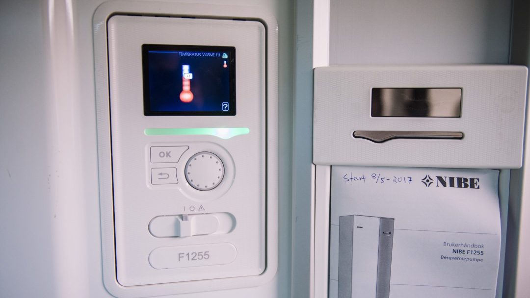 Et kontrollpanel merket F1255 har et temperaturikon på skjermen. Et spor inneholder en bruksanvisning merket NIBE. Et notat sier Satt 9/5-2017, som antyder implementering av energitiltak for effektiv energistyring.