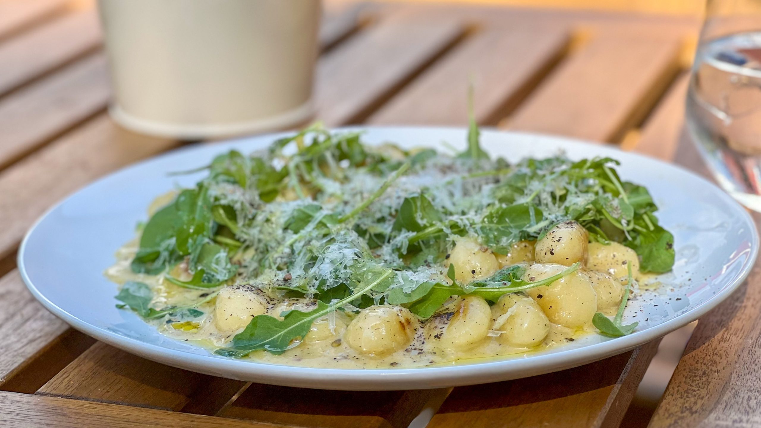 En tallerken med gnocchi toppet med ruccola og revet ost står på et trebord, og inviterer deg til å forestille deg kystreiser i likhet med øyhopping.