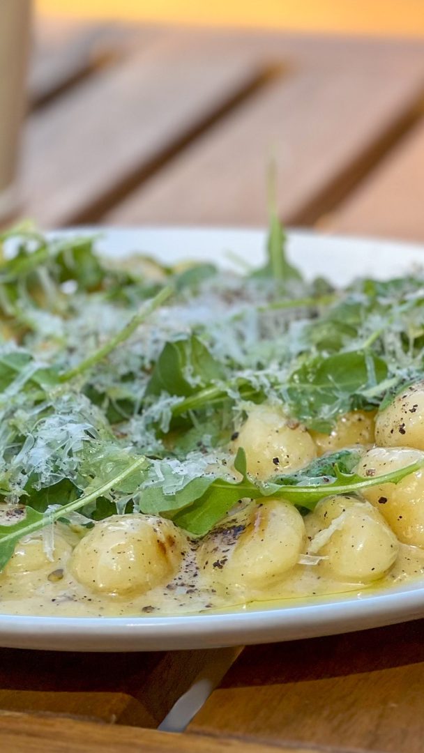 En tallerken med gnocchi pyntet med ruccola, revet ost og sort pepper fremkaller den rustikke sjarmen til et øyhoppeeventyr på et trebord.