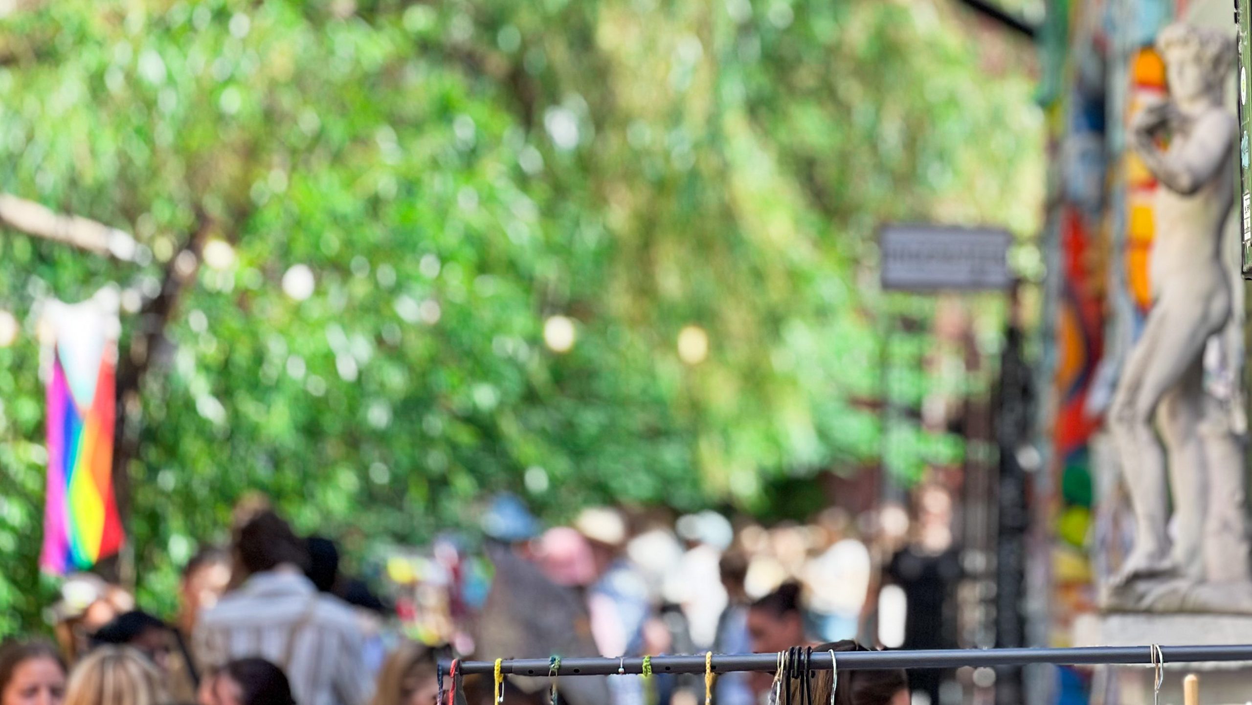 Et overfylt utendørsmarked med uskarpe mennesker i bakgrunnen, en fargerik vegg til høyre og en utstilling av hengende gjenstander i forgrunnen skaper skattejakt-stemning.