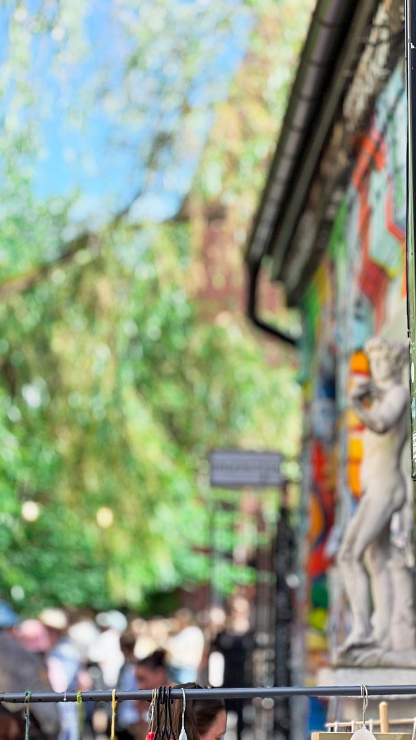 Et gatebilde med fargerik graffiti antyder en skjult skattejakt, med en delvis synlig statue og en uskarp bakgrunn av trær og mennesker.