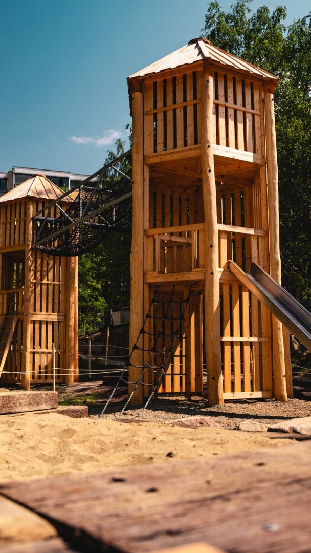 Disse sjarmerende lekeplassene ligger i et sandområde omgitt av trær, og har en trekonstruksjon med to tårn forbundet med en taubro. Barn kan glede seg over spennende sklier og eventyrlige klatrenett, noe som skaper en spennende lekeplassopplevelse for alle aldre.
