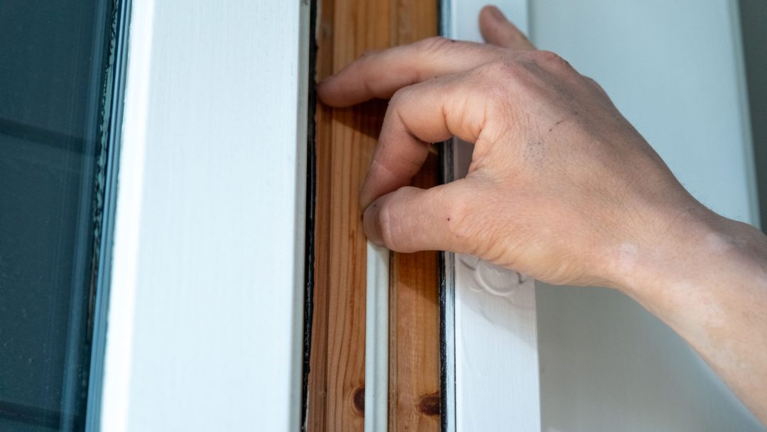 En person justerer forsiktig trefiltråd på kanten av en hvit dør, et energitiltak som tar sikte på å optimere strømeffektiviteten i hjemmet.