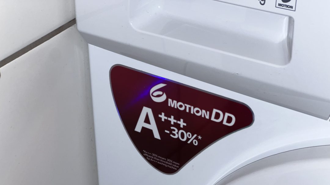 Nærbilde av en vaskemaskin med en rød etikett som viser Motion DD A+++ -30%, som fremhever dens energieffektivitet. Dette energimerket gjenspeiler den overlegne ytelsen og bærekraften som er typisk for moderne elektriske produkter.