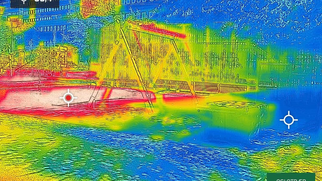 Et termisk bilde fanger en lekeplass midt i trær, med svinger som avslører overflatetemperaturer i livlige farger, fra kjøligere blått og grønt til varmere gult og rødt.