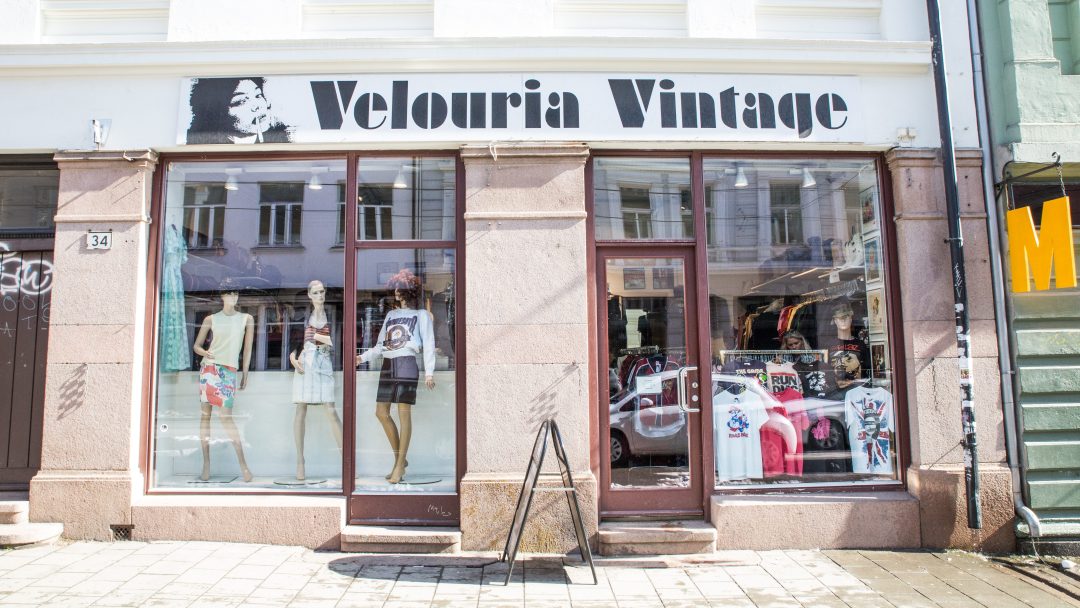 Butikkfronten til Velouria Vintage, en av de sjarmerende bruktbutikkene i byen, med utstillingsdukker kledd i forskjellige antrekk med gateutsikt reflektert i glassvinduene.