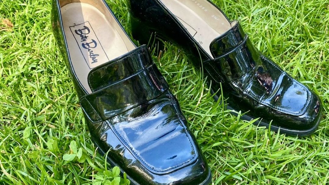 Et par skinnende svarte loafers i skinn med lave hæler, tilfeldig hvilende på grønt gress, kan se kjent ut for de som ofte bruker butikk.