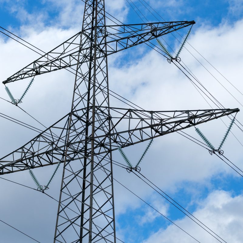 Elektrisitetsmasten står høyt mot en blå himmel med skyer, og symboliserer den sømløse integreringen av energifleksibilitetsmerket i kraftlandskapet vårt.