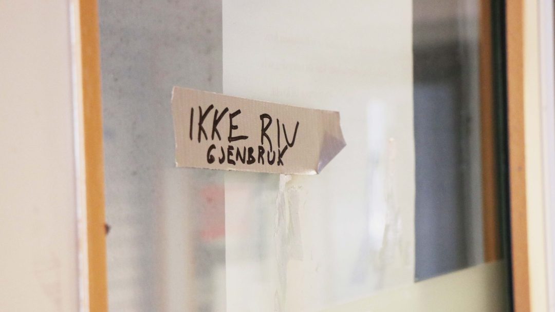 Et stykke tape på en glassflate med håndskrevet tekst på norsk med tekst IKKE RIV, GJENBRUK, og et nikk til viktigheten av klimabudsjettet. Dette minner forbipasserende om bærekraftige valg.