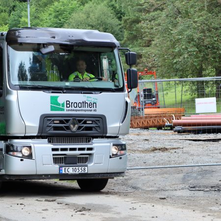 En elektrisk lastebil med Braathen firmalogo står parkert i nærheten av en byggeplass, der gjerder og rør er synlige i bakgrunnen.