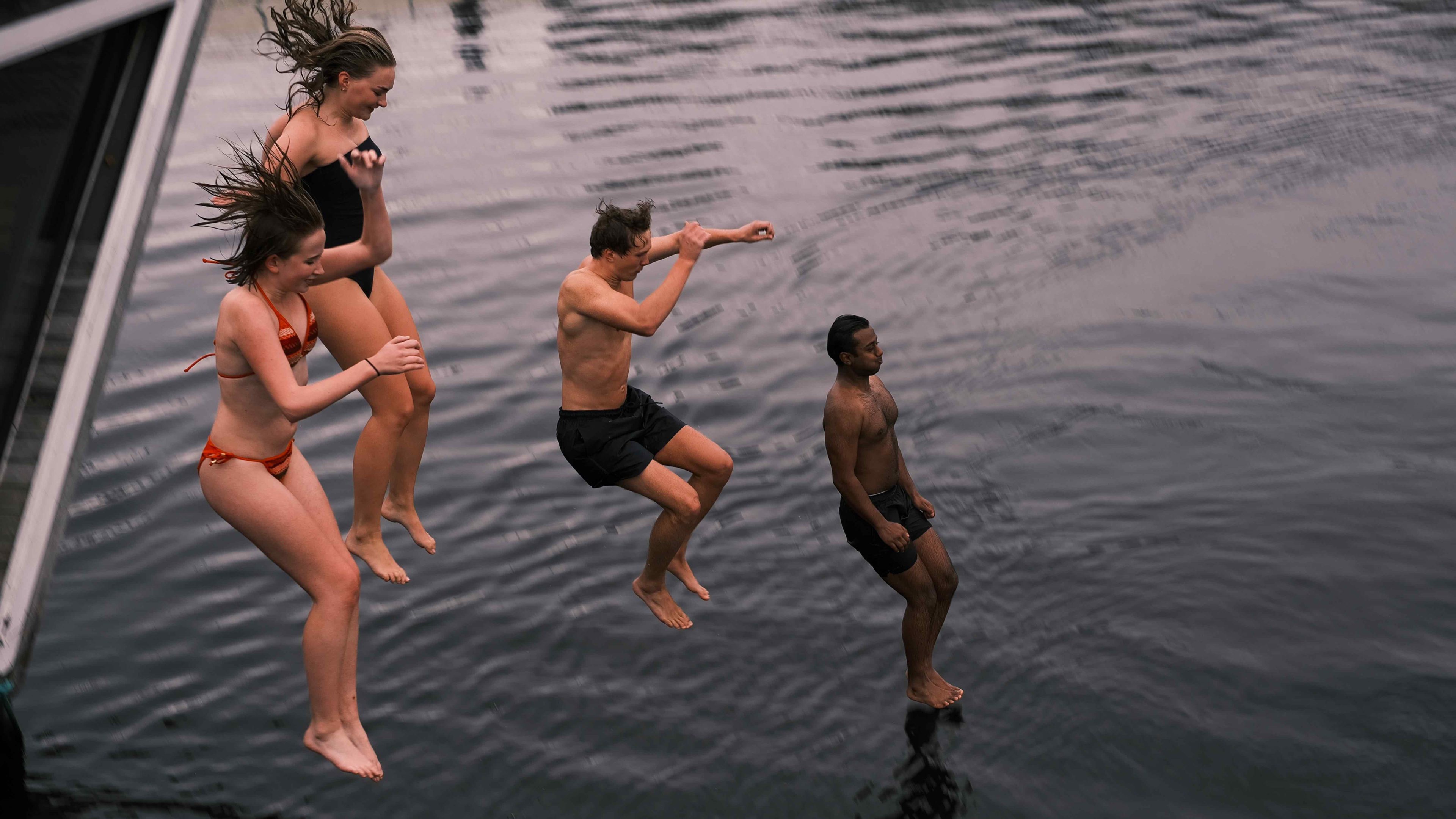 fire unge voksne som hopper i sjøen fra badstu