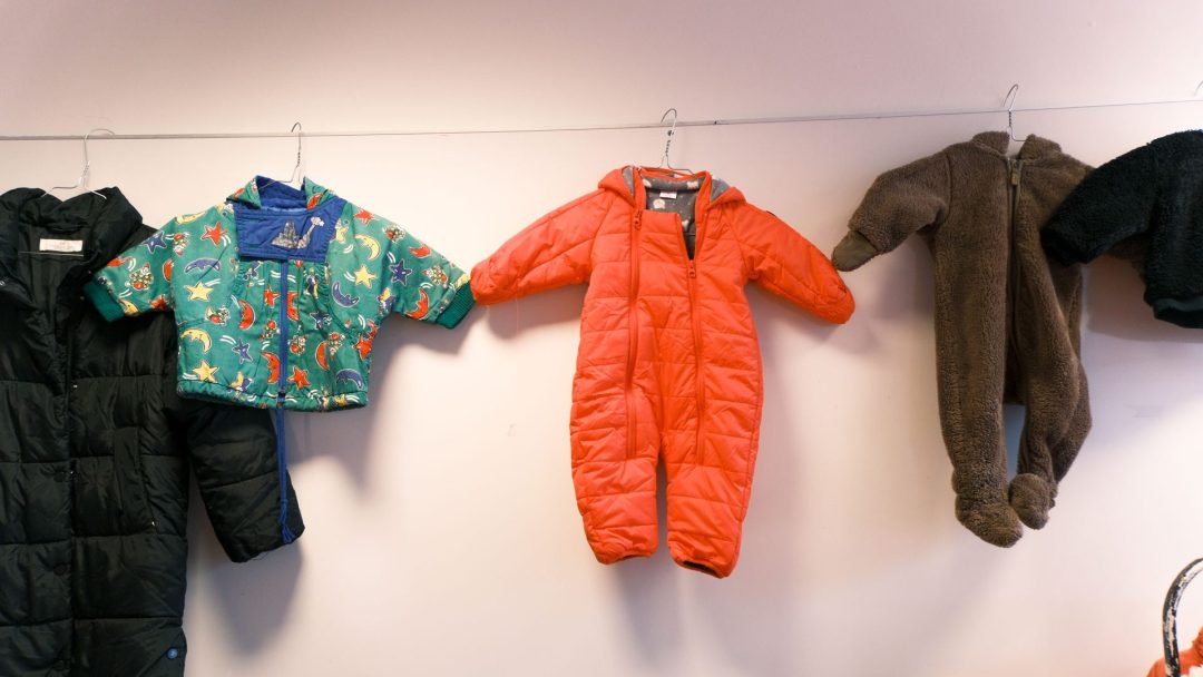 På loppemarked henger vinterklær for barn som grønnmønstret antrekk, rød snødrakt, dress med brun bjørnetema og svart antrekk på strek.