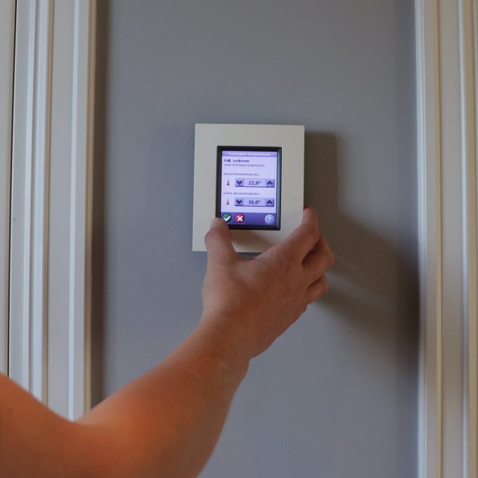 En person justerer en smart termostat med digitalt display, viser temperatur og strømstyringsmuligheter for effektiv kontroll.