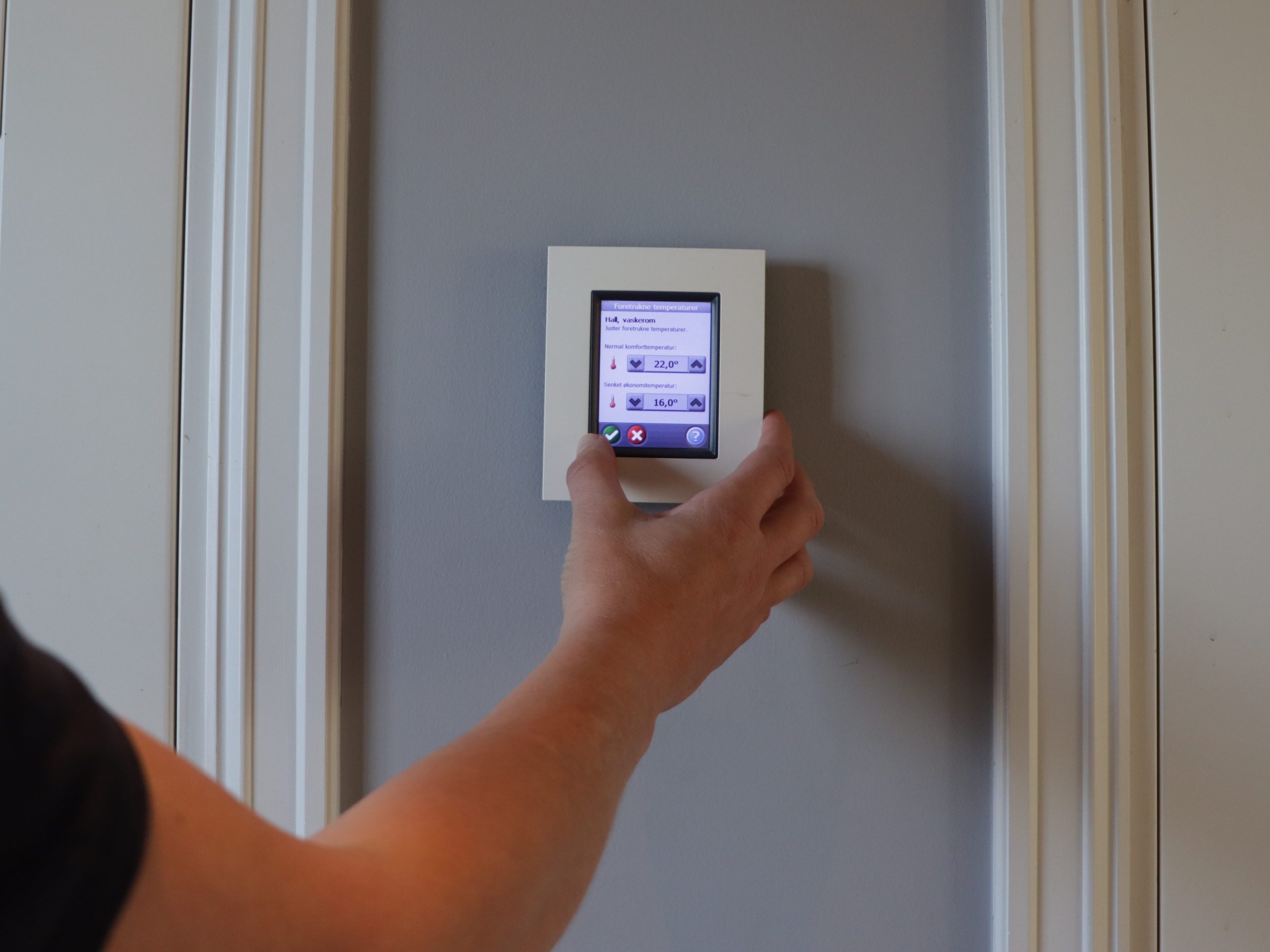 En person justerer en smart termostat med digitalt display, viser temperatur og strømstyringsmuligheter for effektiv kontroll.