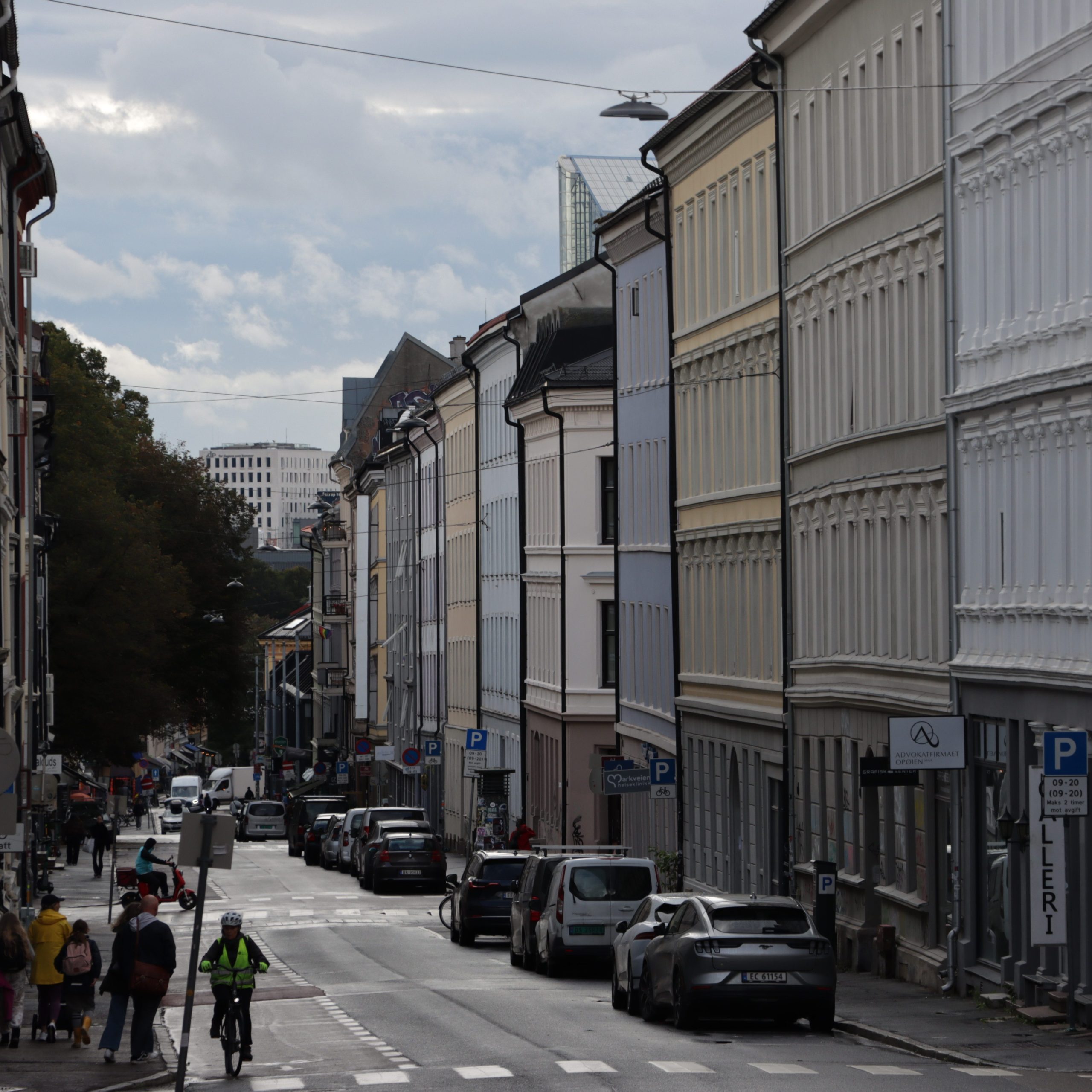 Gateutsikt med pulserende rekkehus fra Byantikvarens Gul liste, parkerte biler og en syklist som navigerer den våte veien. Den overskyede himmelen ruver over hodet mens fotgjengere rusler på fortauet.