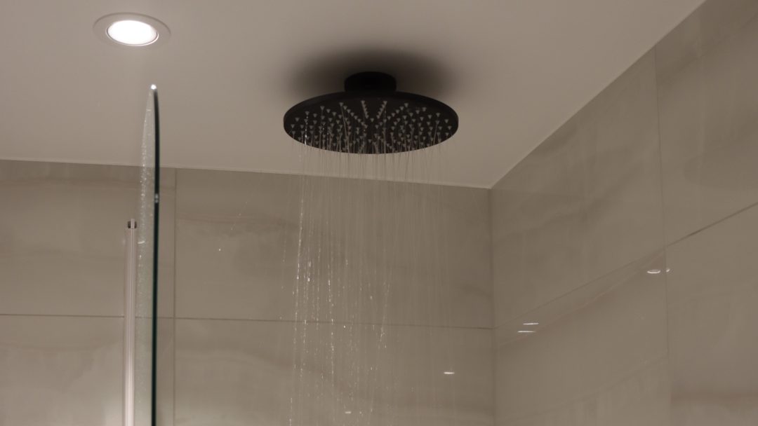 Et moderne strøm takdusjhode med rennende vann, installert i et flislagt baderomstak for optimal sparring og eleganse.
