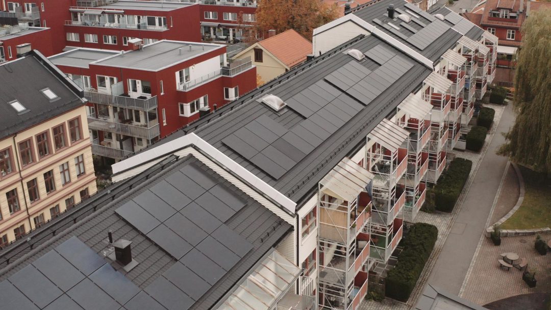 En rad med bolighus med solcelleanlegg på hustakene, i et urbant nabolag med trær og stier.