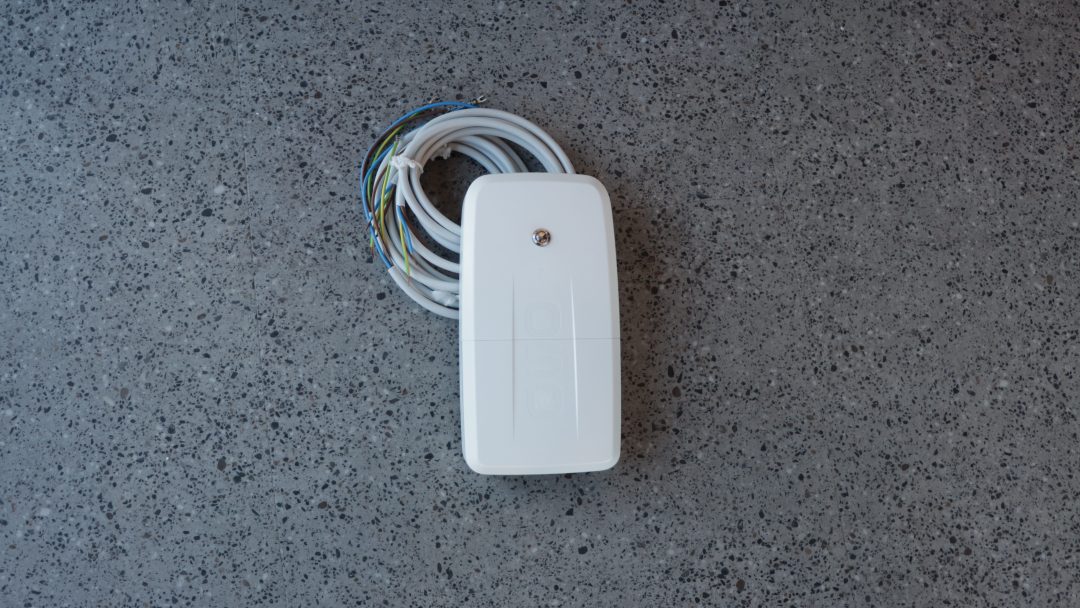 En hvit elektrisk enhet med smarte strømstyringsmuligheter og flerfargede ledninger hviler på en flekkete grå overflate.