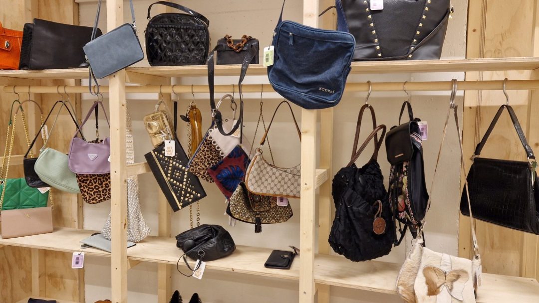 Hyllene i bruktbutikken viser en rekke håndvesker, clutcher og vesker, som hver har unike farger og stiler.