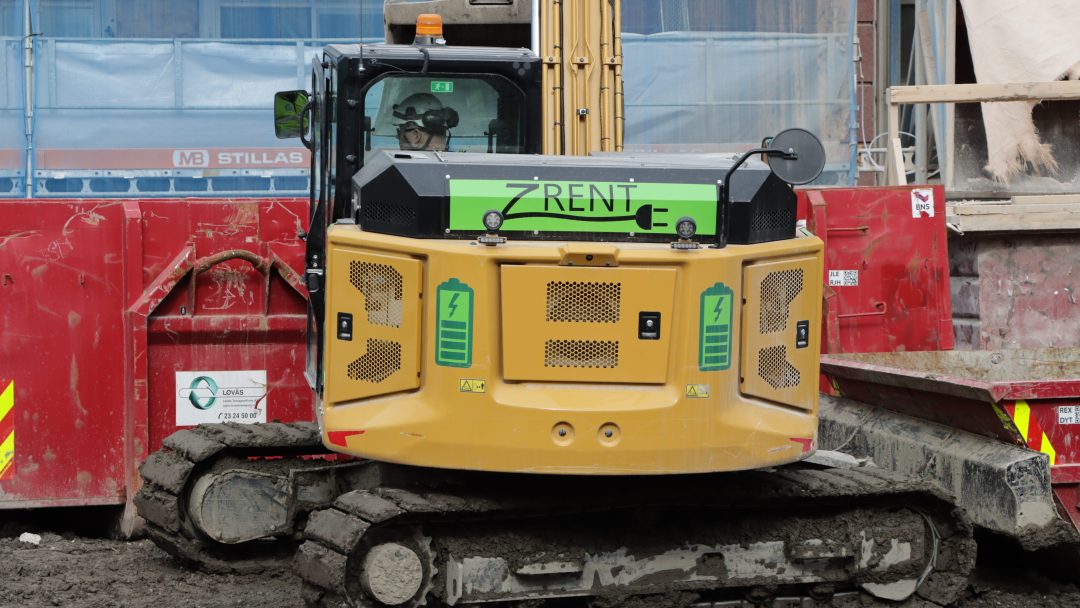 Et grønt og svart anleggskjøretøy merket ZRENT opererer effektivt på stedet, blant røde barrierer og skitt, og viser viktigheten av strategiske anskaffelser i moderne utviklingsprosjekter.