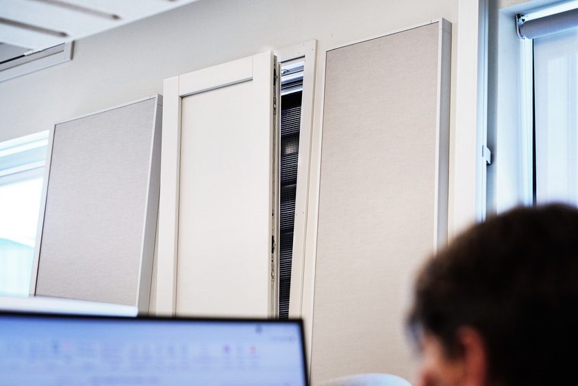 Akustikkpaneler fra Vertikal Nydalen pryder kontorveggen, mens en dataskjerm og toppen av en persons hode titter inn i forgrunnen.