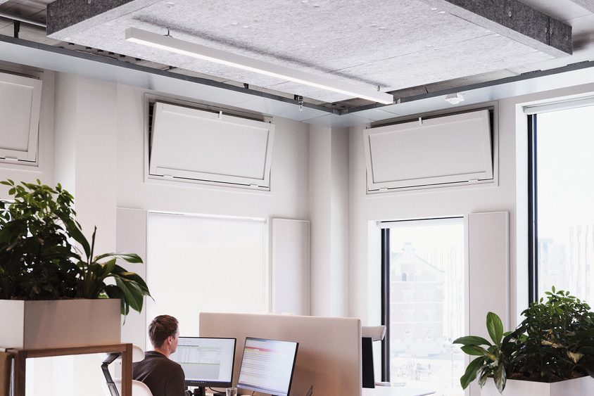 I det pulserende kontorlokalet i Vertikal Nydalen jobber en person flittig ved en pult utstyrt med doble monitorer. Sollys strømmer inn gjennom store vinduer, varmer rommet og gir næring til de frodige innendørsplantene som gir et naturpreg til denne moderne arbeidsplassen.