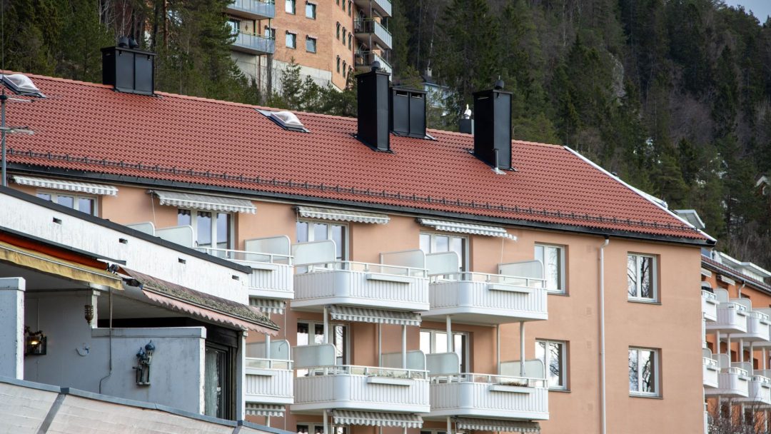 Leilighetsbygg med røde tak og balkonger, med energieffektive vinduer, ligger omgitt av trær og kupert terreng.