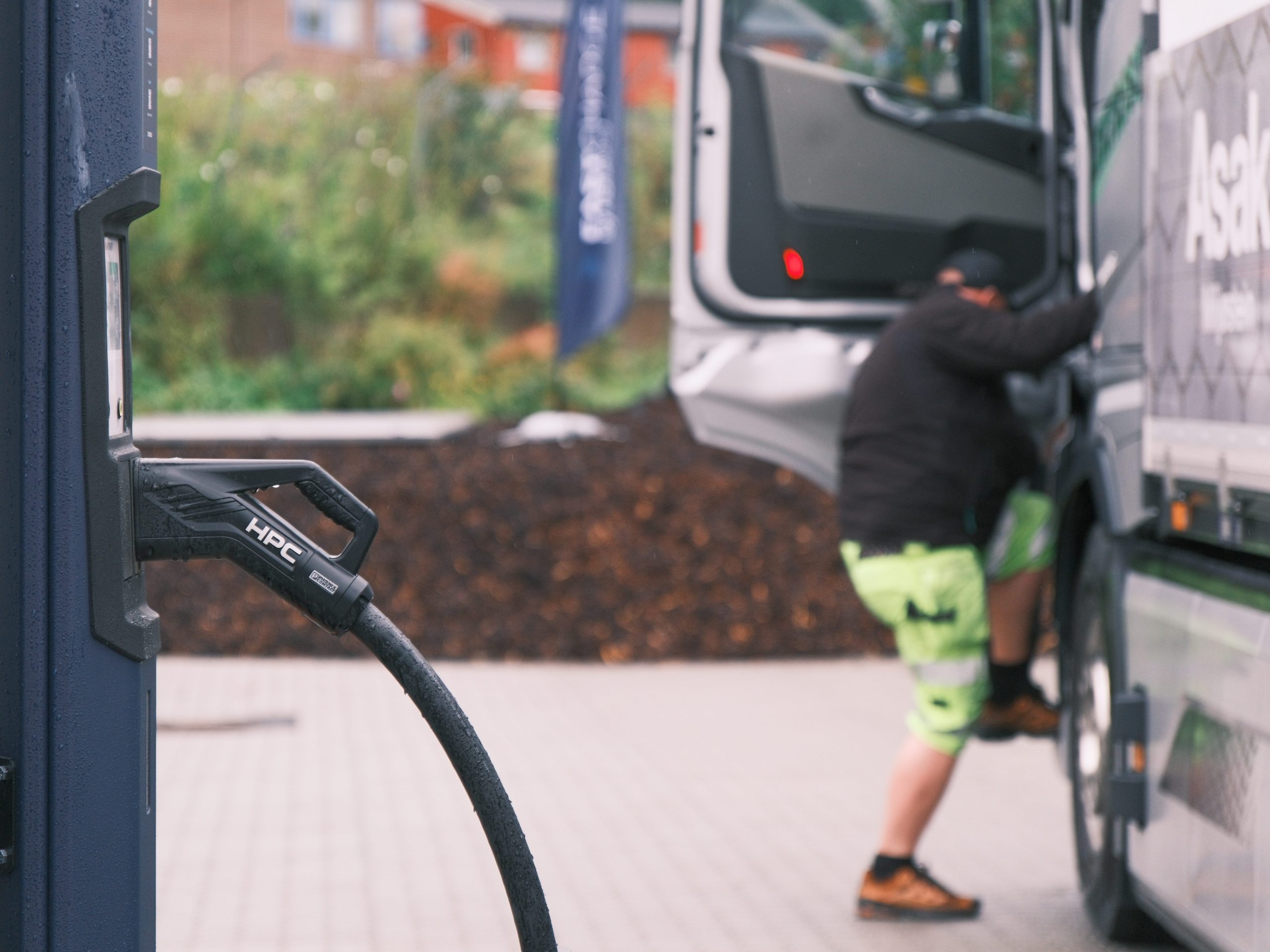 En person i knallgrønne shorts klatrer inn i en lastebil, med en hurtigladestasjoner synlig i forgrunnen.