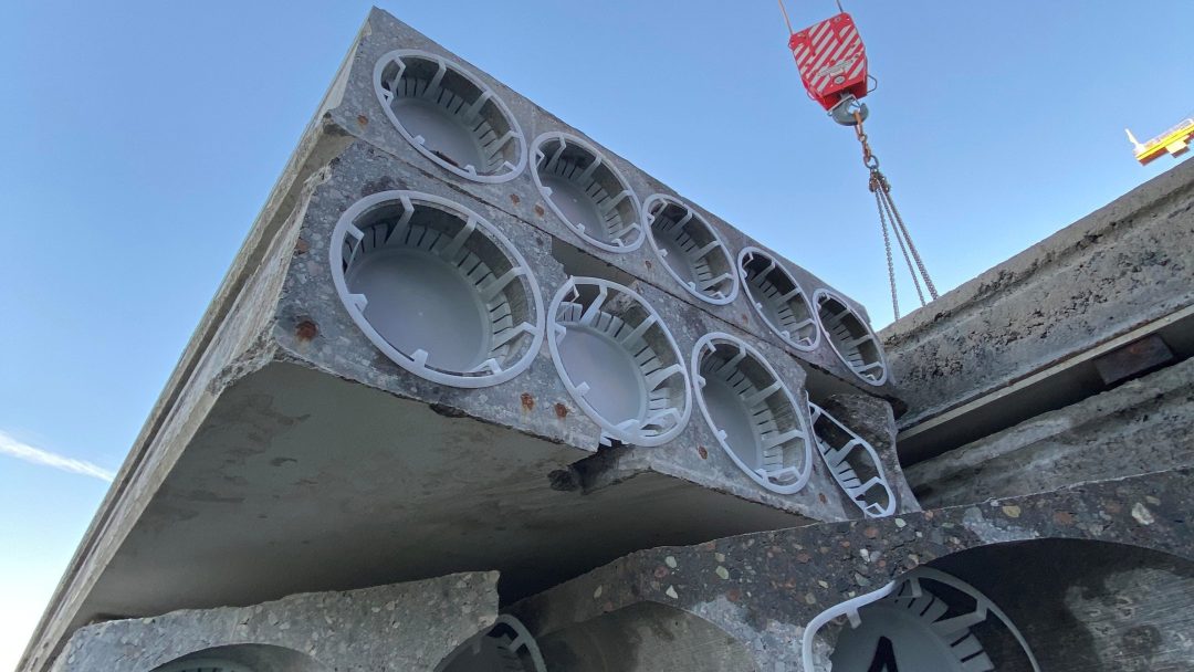 Betongplater, essensielle bygningsmaterialer, løftes med kran. Disse robuste platene har sirkulære åpninger.