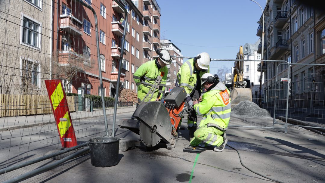Emission-free machines: Three men in yellow workwear are working cutting asphalt in a street. Utslippsfrie maskiner: Tre menn i gule arbeidsklær jobber med å sage i asfalten i en vei