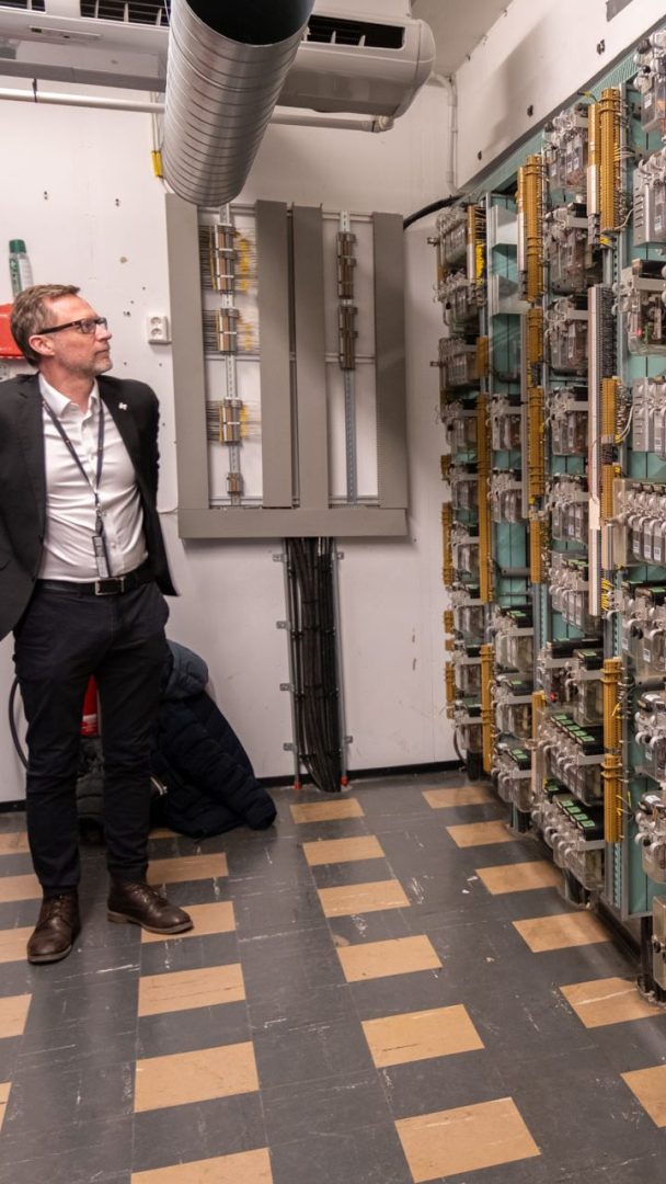 En person i kontorantrekk står i et rom fylt med høye stativer med dataservere og elektronisk utstyr.