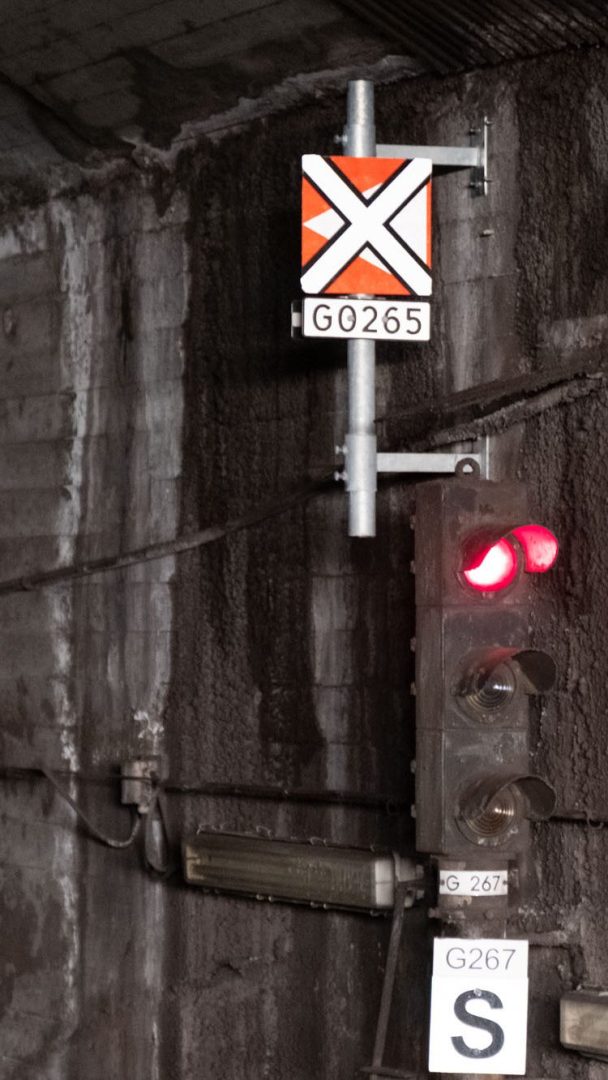 Rødt jernbanesignal med to tente lamper i en tunnel. Skiltene leser G0265 med en X og G267 S. Rusten, strukturert veggbakgrunn.
