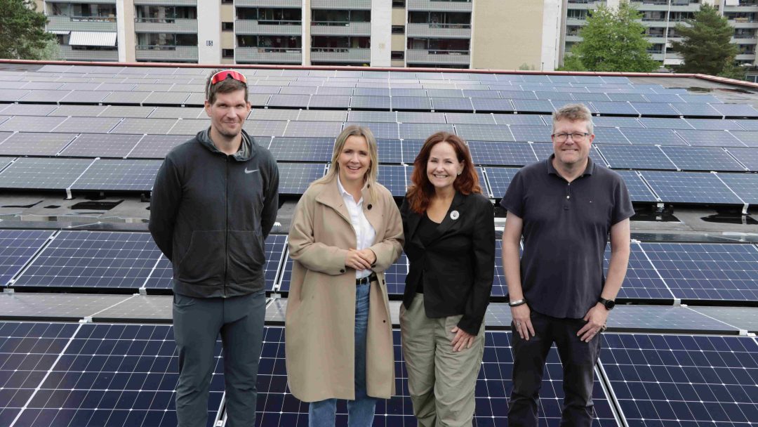 Fire personer står på et tak, foram anlegget som produserer solenergi