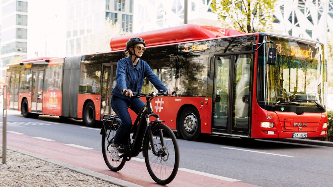person sykler i bygate på elsykkel, ved siden av en buss