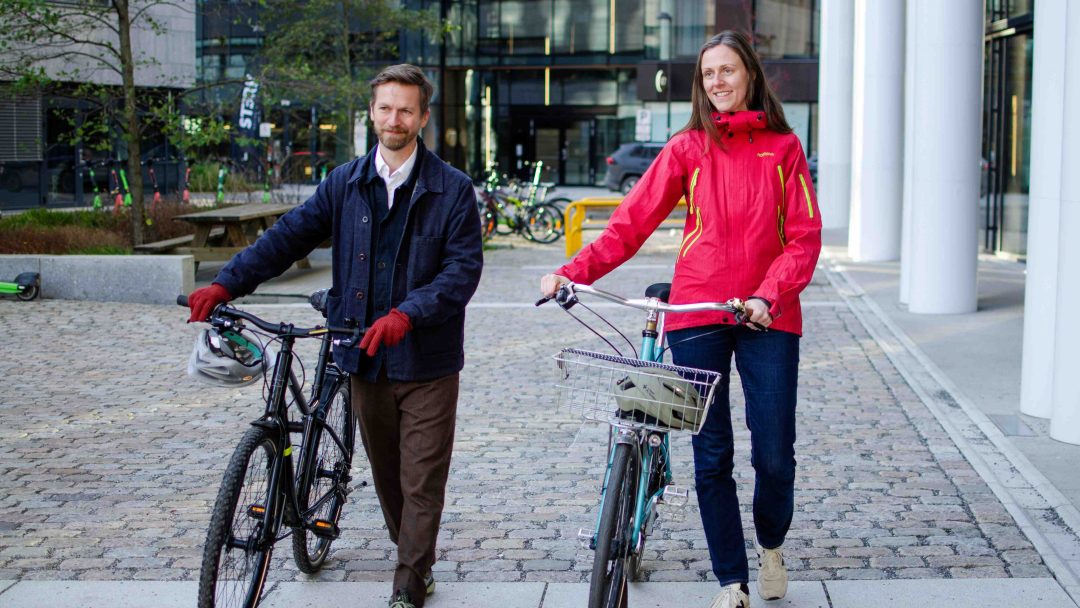 En mann og en kvinne triller hver sin sykkel over en plass belagt med brosten