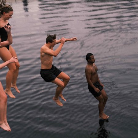 fire unge voksne som hopper i sjøen fra badstu