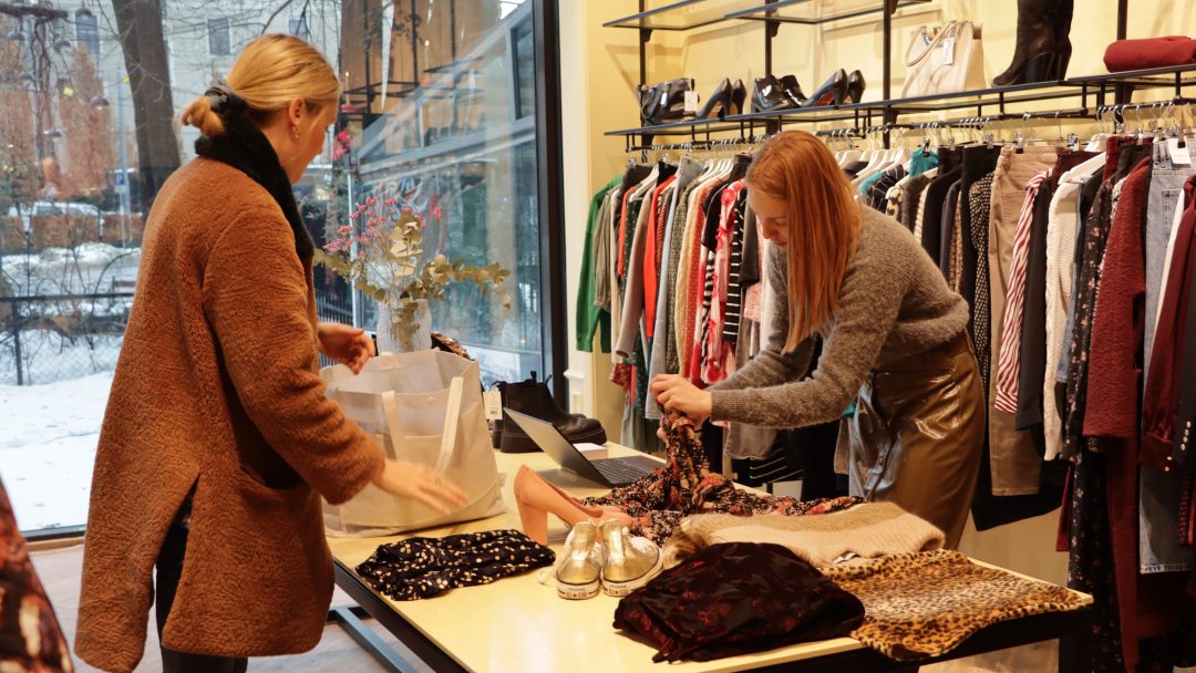 To kvinner, en kunde og en ansatt, står ved disken i en bruktbutikk der du både kan kjøpe og selge brukte klær i Oslo.
