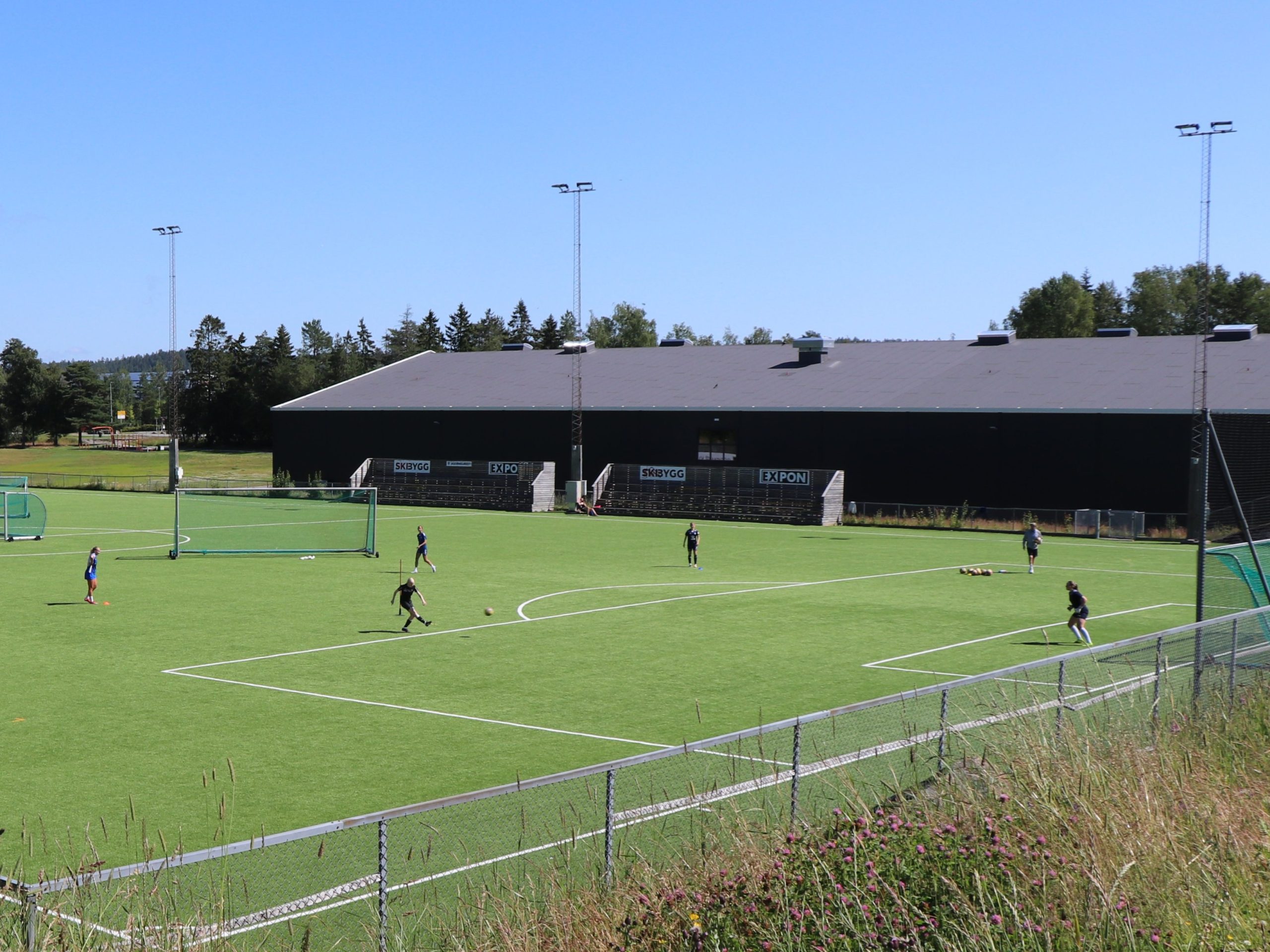 fotballspillere trener på kunstgressbane i sollys og blå himmel