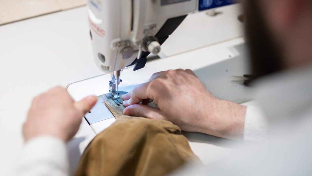 Nærbilde av hender som jobber med en symaskin. En systue eller skredder i Oslo kan hjelpe deg med mer enn du tror