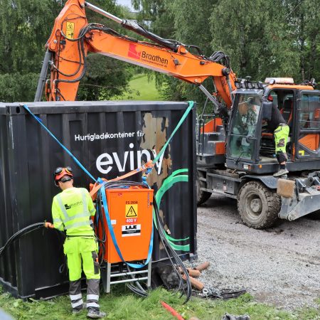A man in front of a charging container at an electric construction site. An electric excavator is in the background.