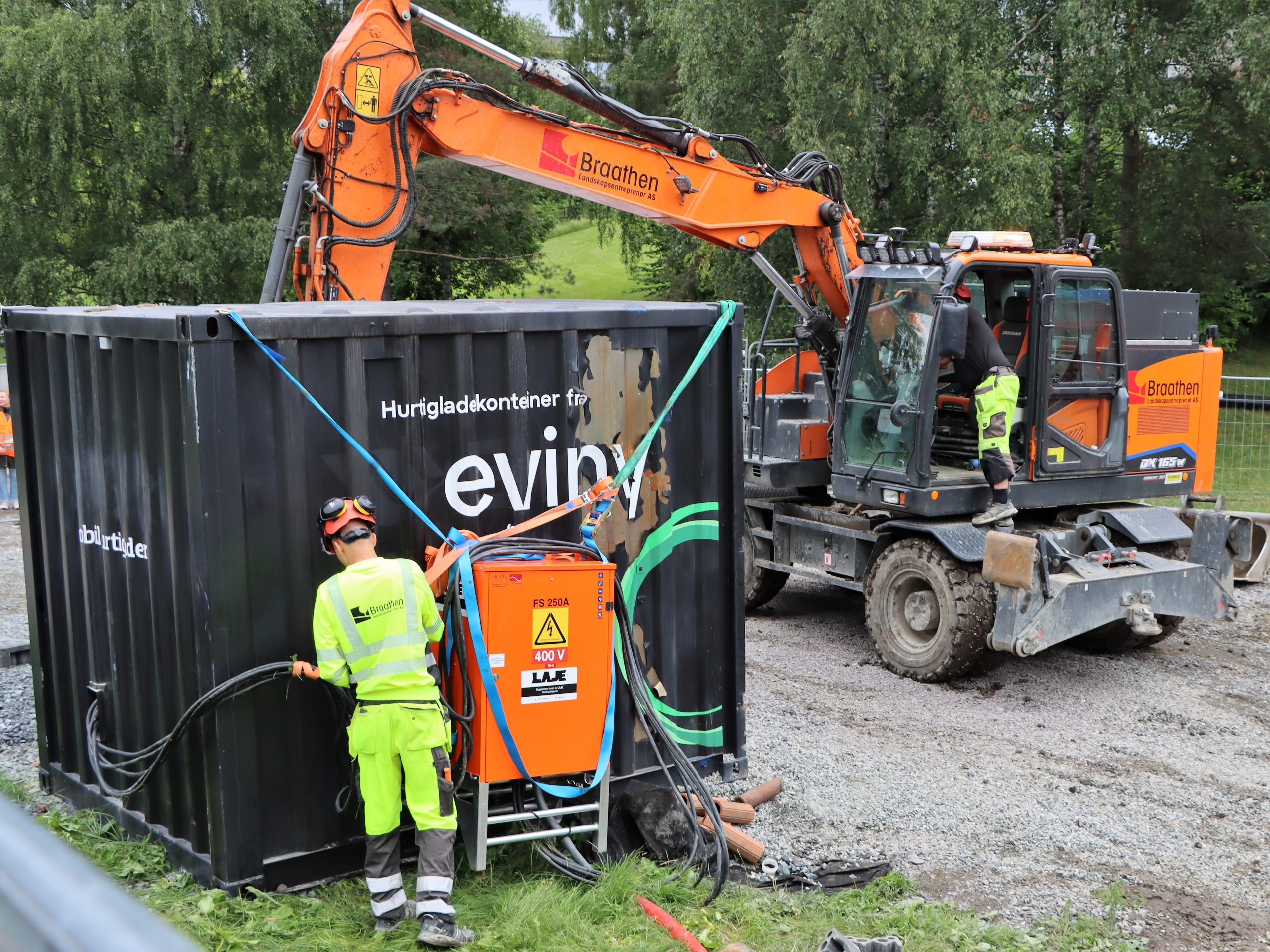 A man in front of a charging container at an electric construction site. An electric excavator is in the background.